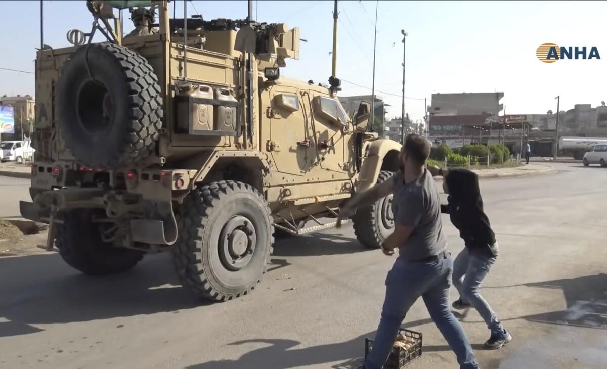 In this frame grab from video provided by Hawar News, ANHA, the Kurdish news agency, residents who are angry over the U.S. withdrawal from Syria hurl potatoes at American military vehicles in the town of Qamishli, northern Syria, on Monday.