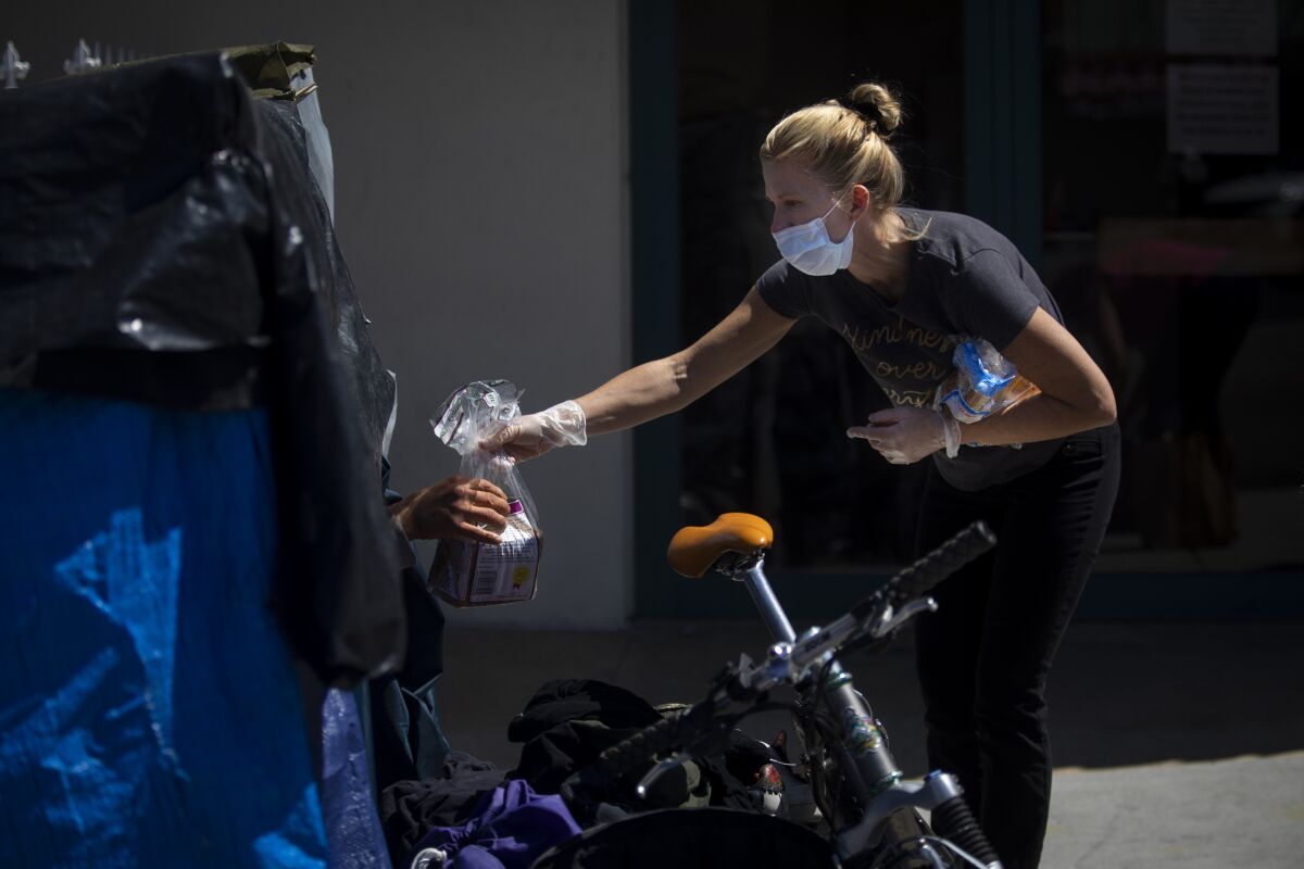 Heidi Roth, a registered nurse, hands bread to a man living in an encampment on a Los Angeles sidewalk. She and others are asking if anyone is experiencing coronavirus symptoms.