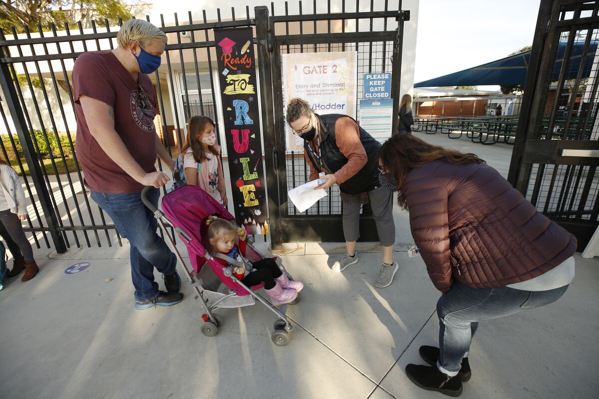 A man pushing a stroller with a toddler in it stands alongside a girl and two school workers.