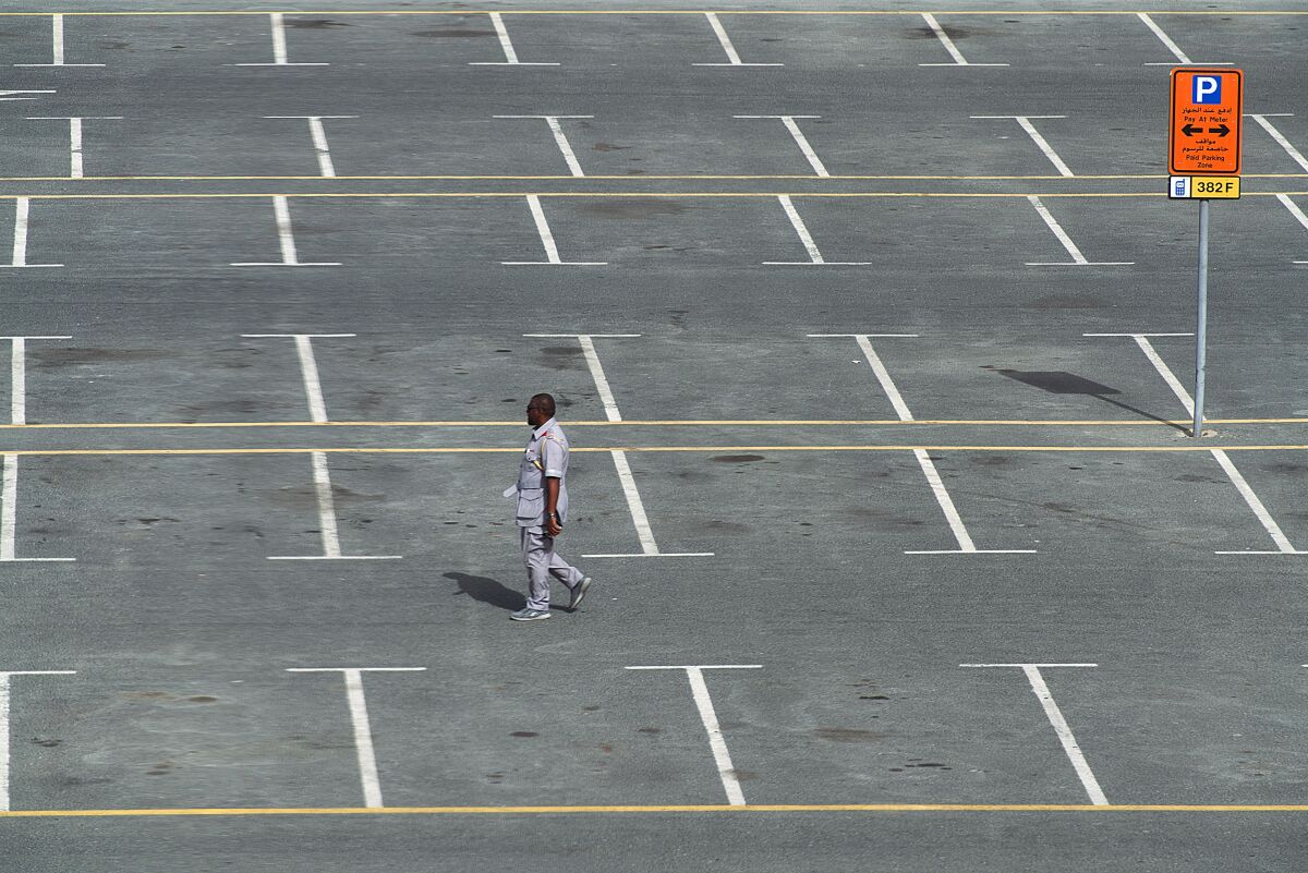 A parking lot attendant walks through a typically full parking lot now largely empty over people staying home due to the worldwide coronavirus pandemic in Dubai, United Arab Emirates, Monday, March 16, 2020. For most people, the new coronavirus causes only mild or moderate symptoms. For some it can cause more severe illness. (AP Photo/Jon Gambrell)