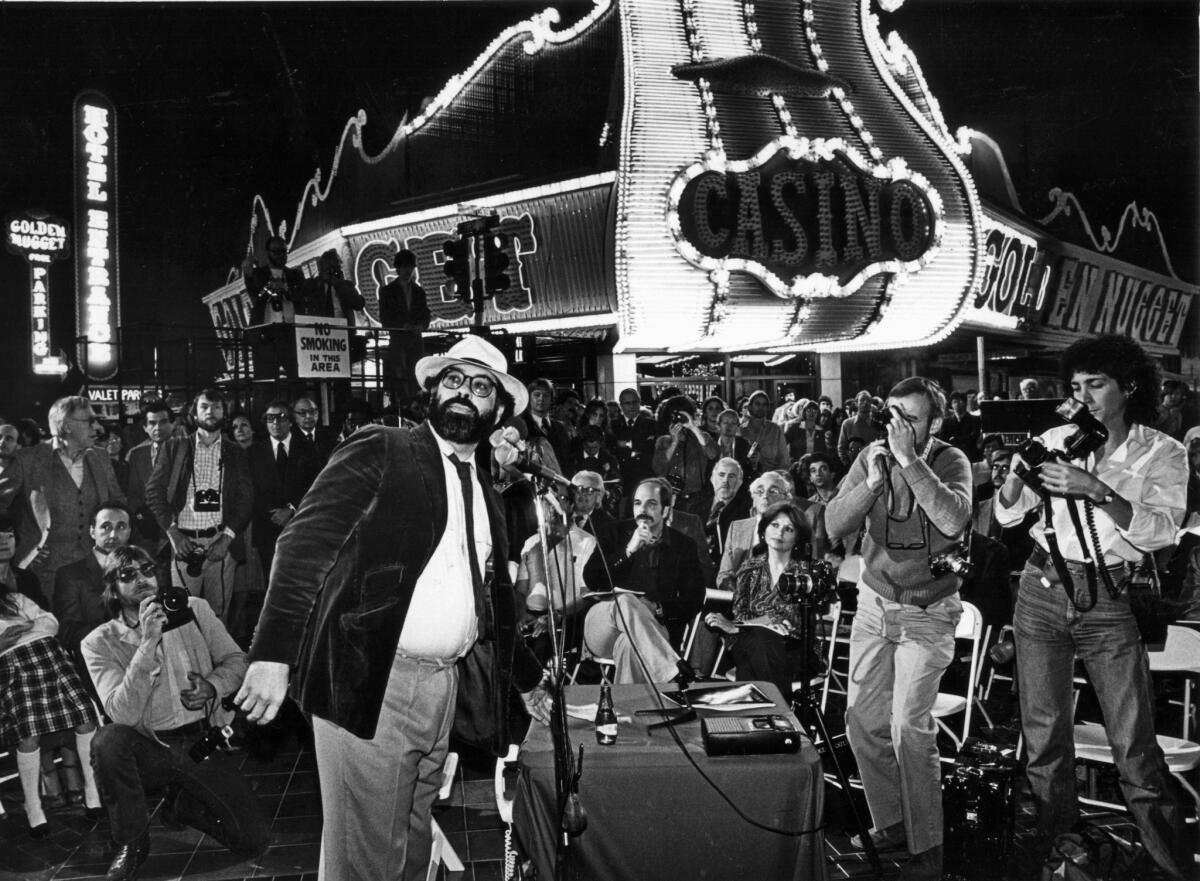 Francis Ford Coppola giving a press conference in Las Vegas in a black-and-white photo in front of a Las Vegas casino.