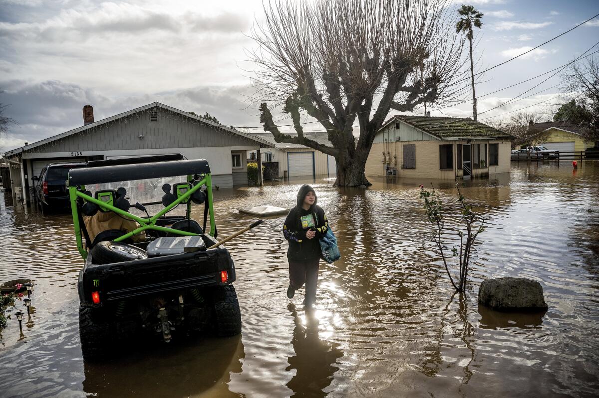 A young woman walks through floodwaters next to a car in front of a home.