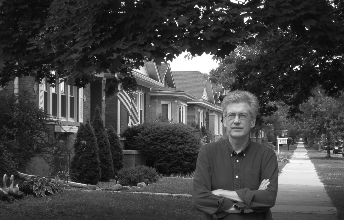 A black-and-white photo of a man on a sidewalk outside homes 