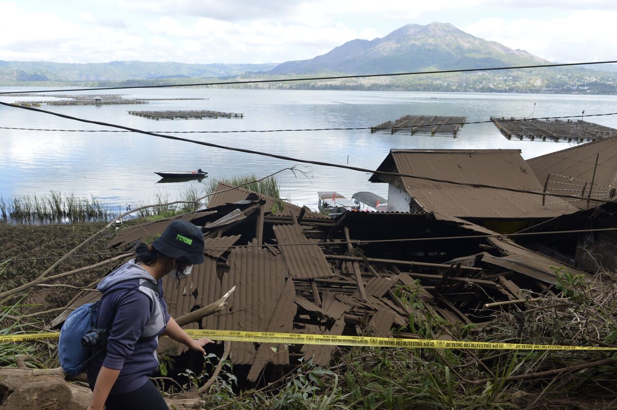 A woman walks past houses by Lake Batur which were damaged by an earthquake-triggered landslide in Bangli, on the island of Bali, Indonesia, Saturday, Oct. 16, 2021. A few people were killed and another several were injured when a moderately strong earthquake and an aftershock hit the island early Saturday. (AP Photo/Dewa Raka)
