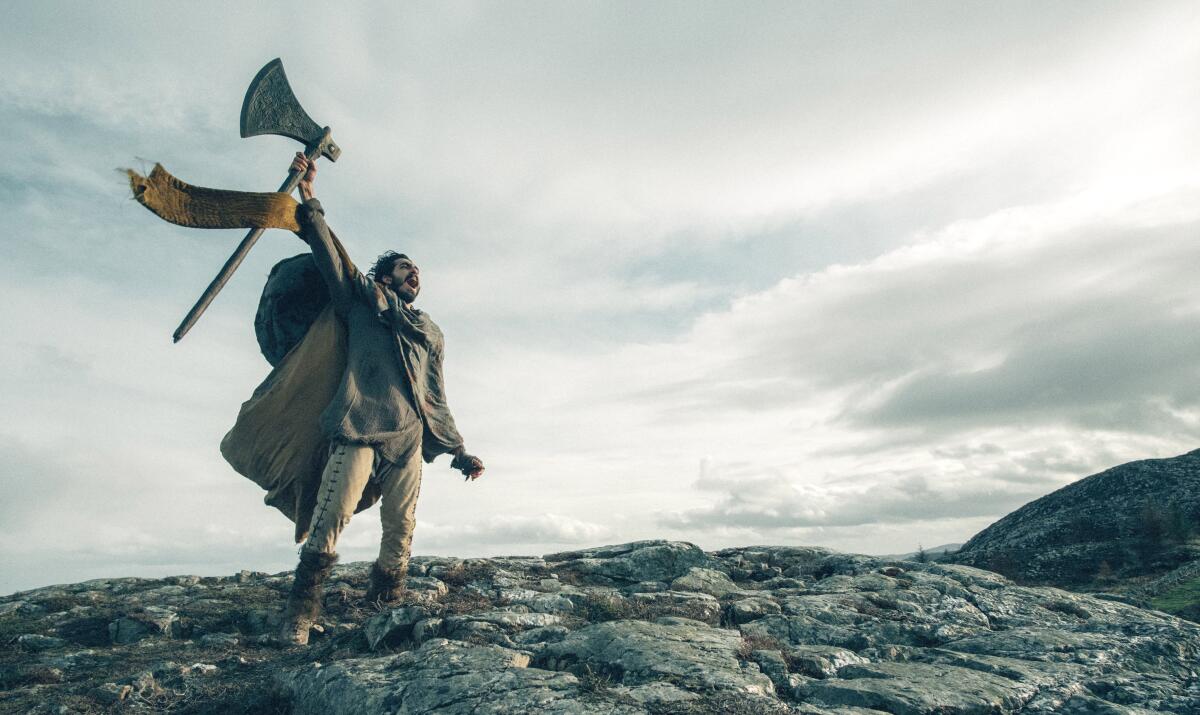 A man standing atop a rocky hill hollers and holds aloft a large ax