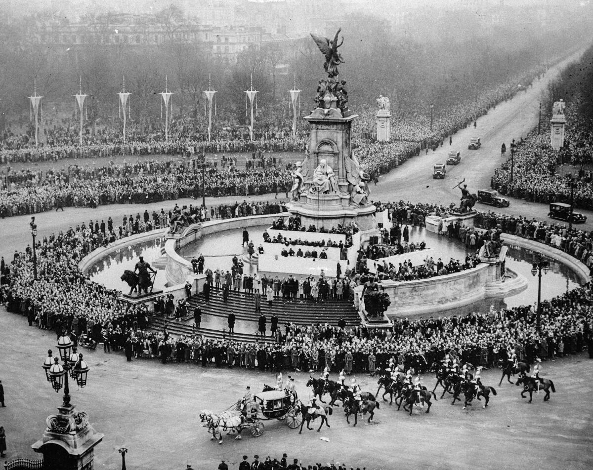 Escorted by a troop of Household Cavalry, the coach circles the Victoria Memorial and heads for the gates of Buckingham Palace, lower left.