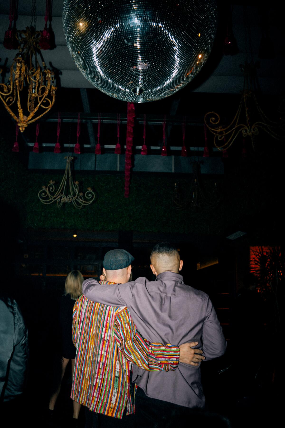 Two men hugging on the dance floor of a nightclub above a disco ball