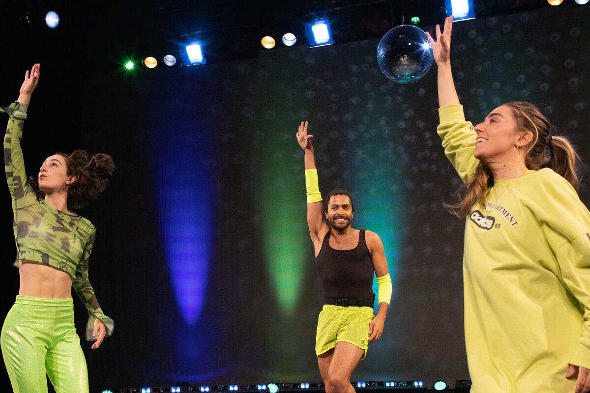 Three people each raise one hand while dancing onstage. 