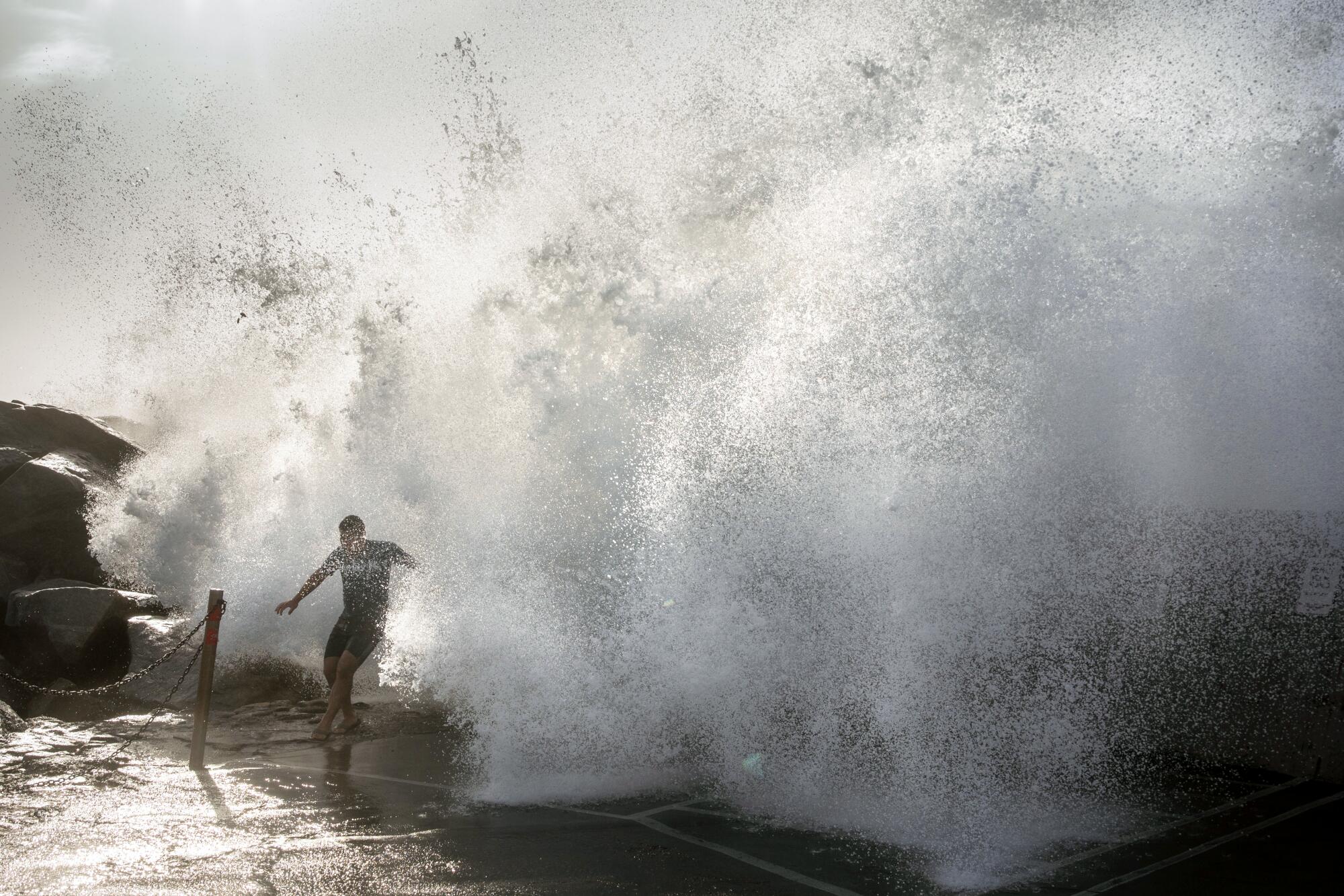 A teen boy runs as large wave comes crashing over a breakwall.