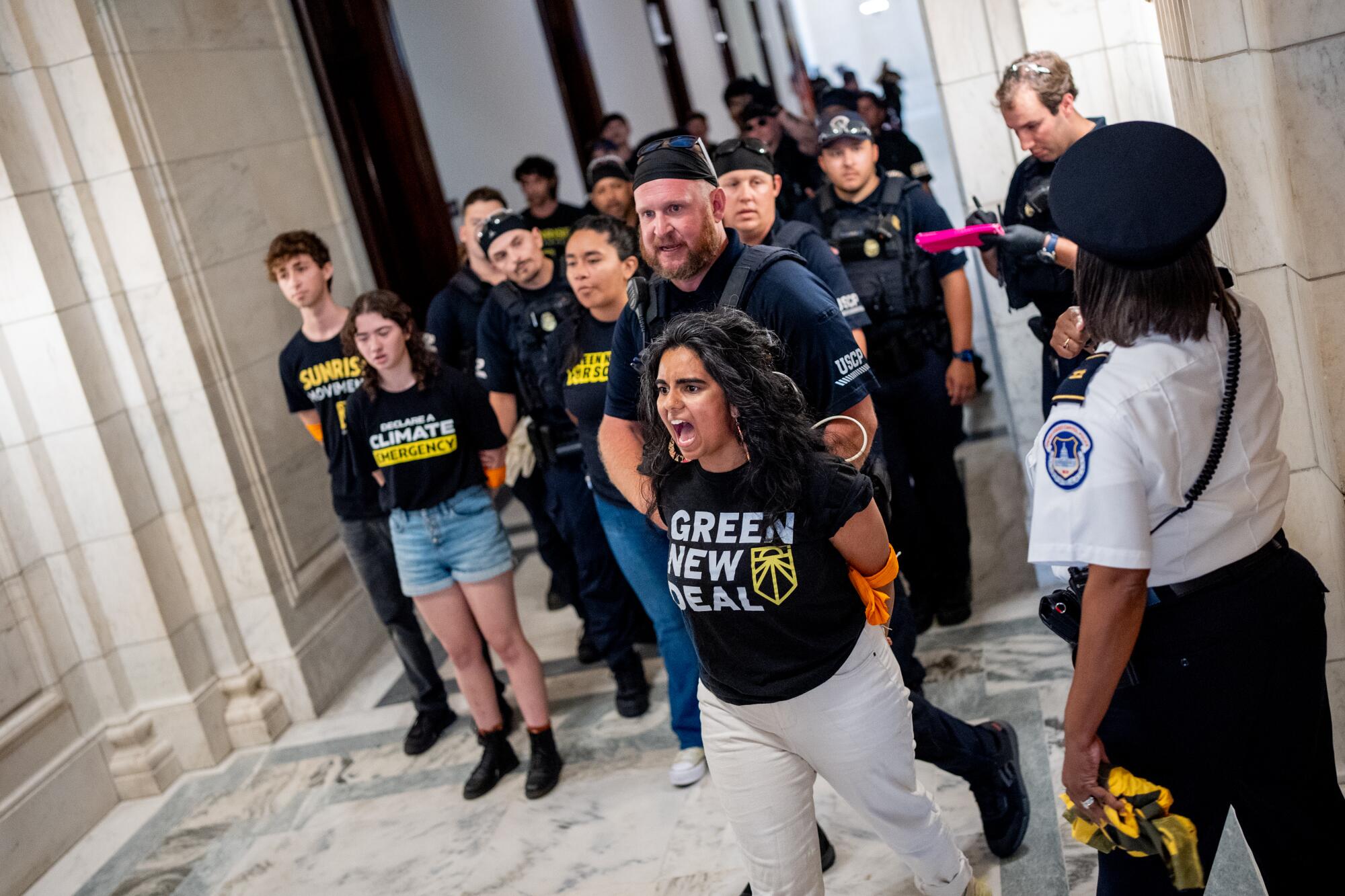 A woman with her hands tied screams as she is escorted past a group of other people.