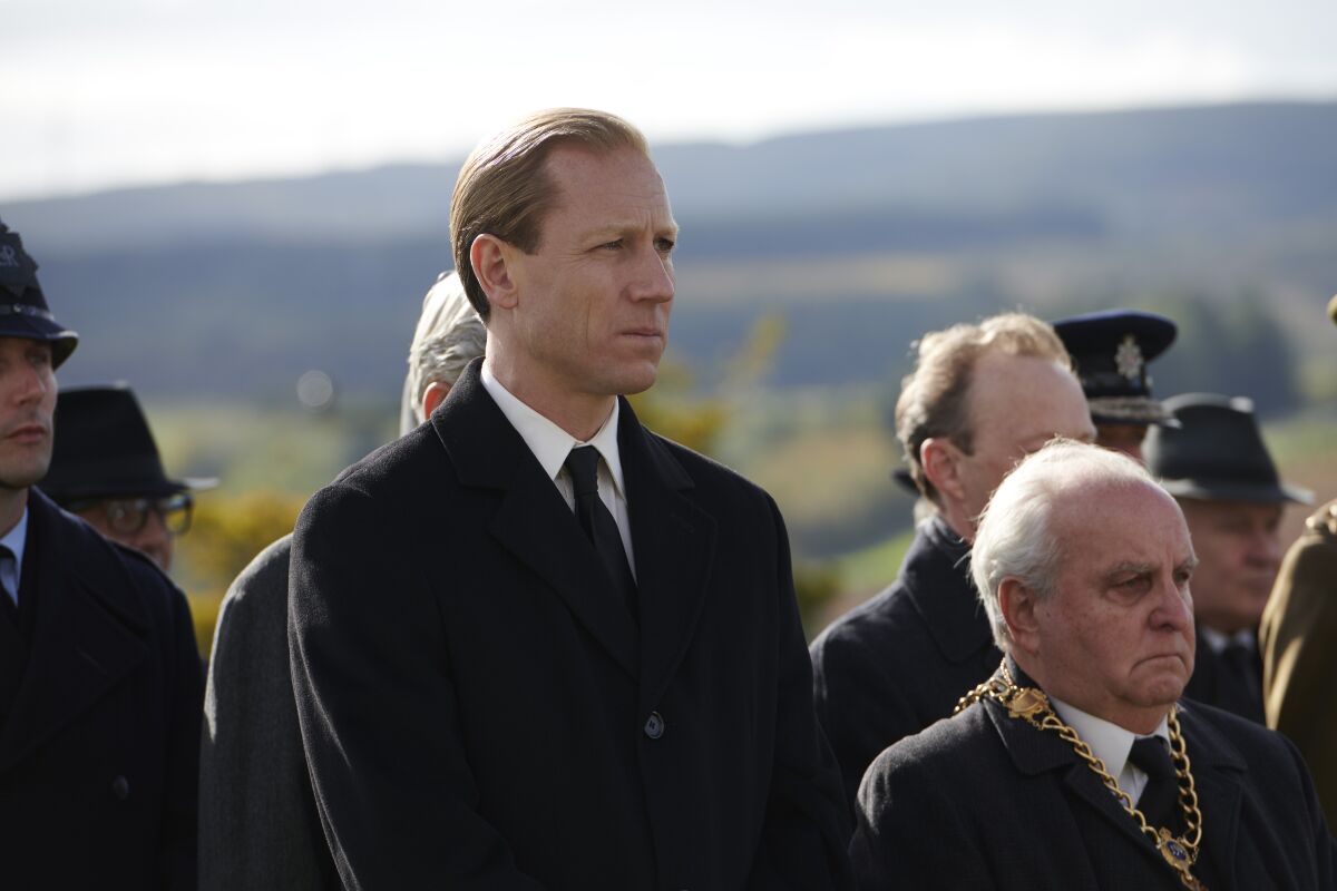 Tobias Menzies as Prince Philip, standing in a small crowd