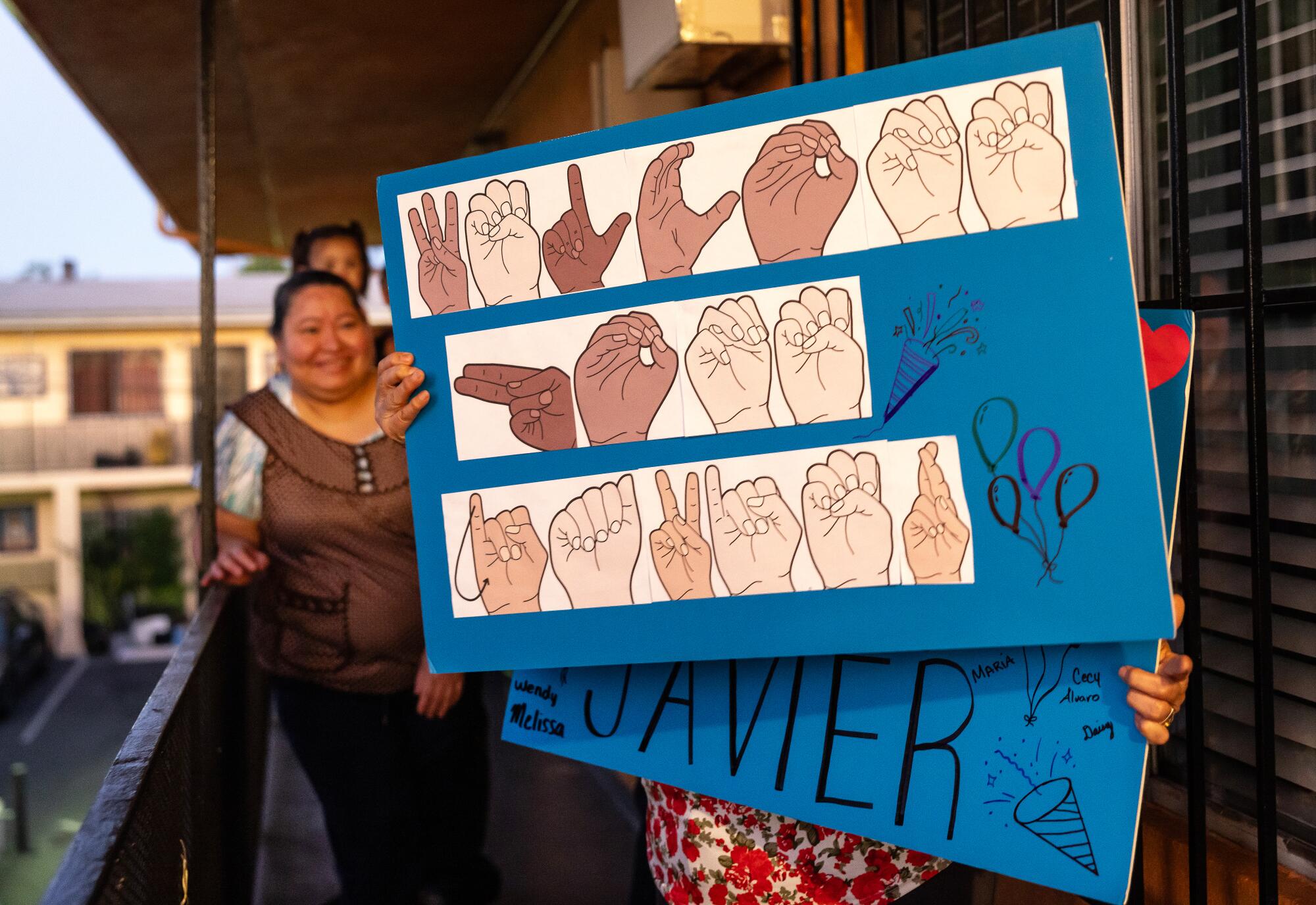 People hold a sign with letters formed as sign language on a balcony