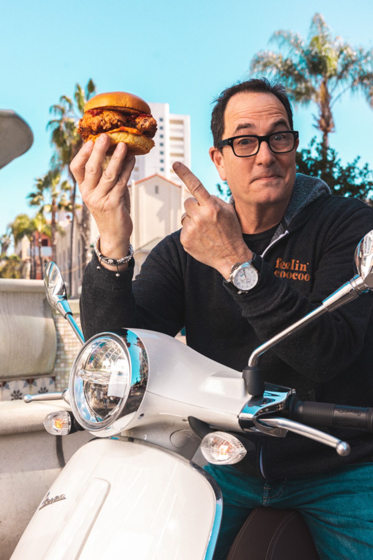 Sam "The Cooking Guy" Zien on a Vespa holding a fried chicken sandwich