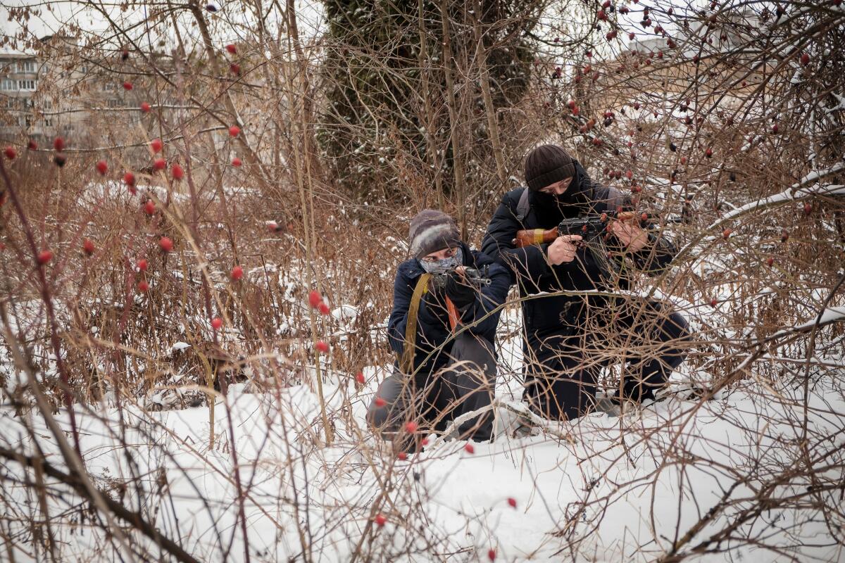 Two people crouch in the snow with guns.