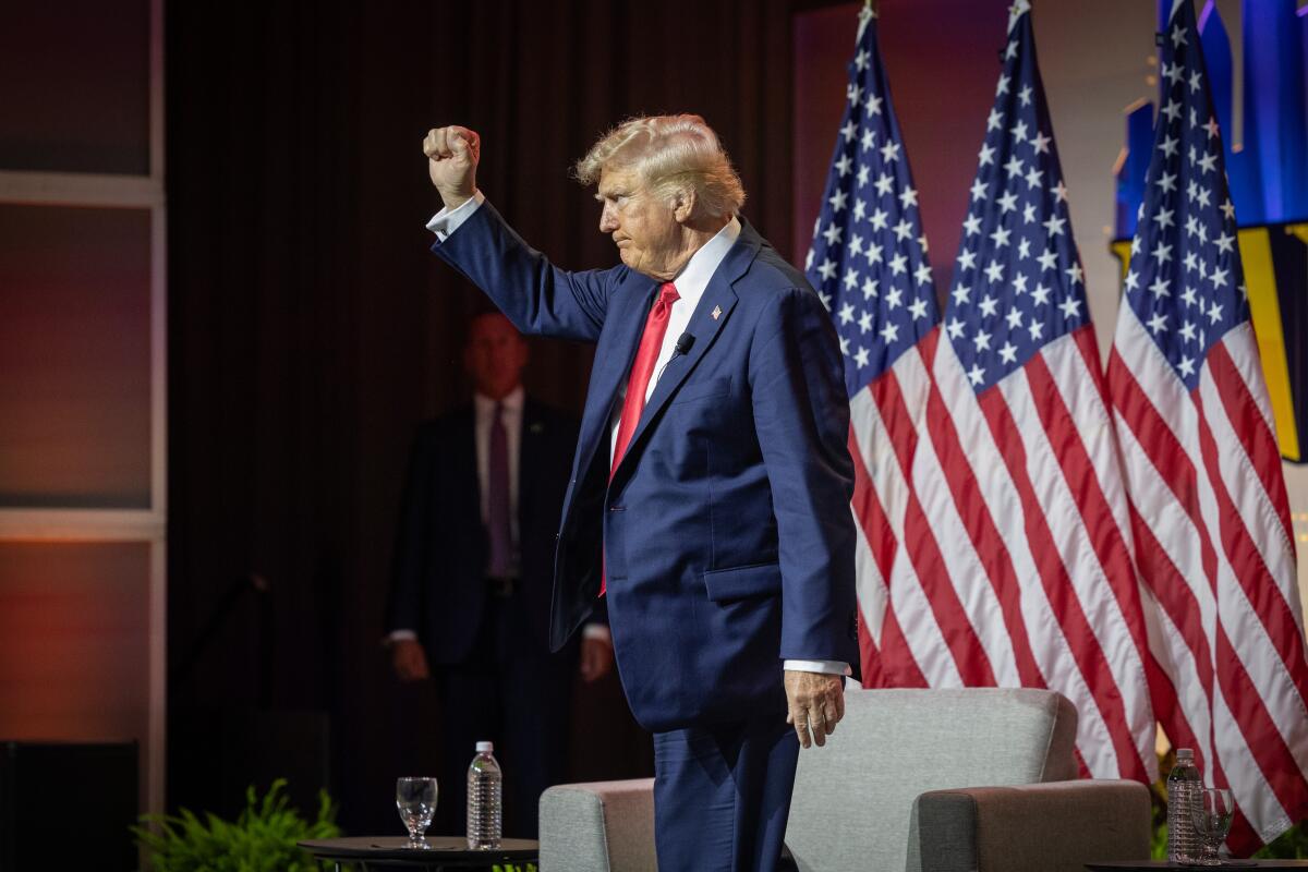 Former President Trump raises his arm with a clenched fist at the NABJ convention.