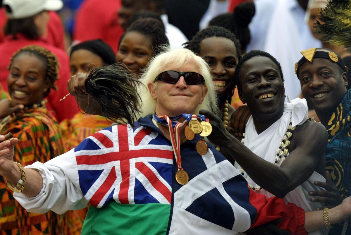 BBC television presenter Jimmy Savile poses with people representing British Commonwealth countries during Golden Jubilee celebrations in London in 2002.