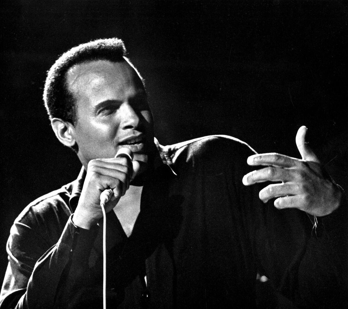 Harry Belafonte holds a microphone and gestures.