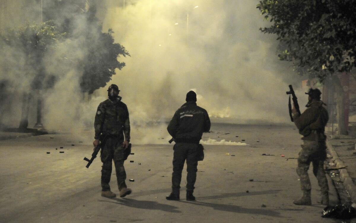 Three police officers stand on a smoke-shrouded street.