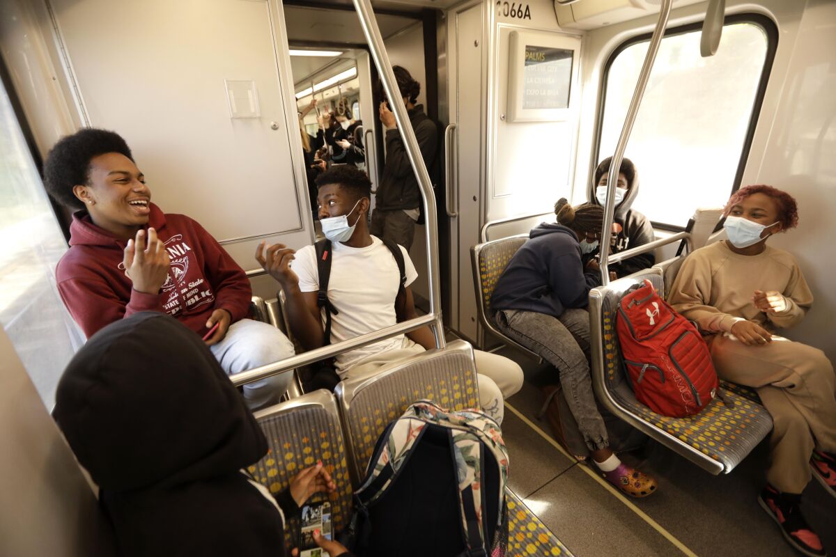 Young people sit on a bus, chatting and laughing; several wear masks.