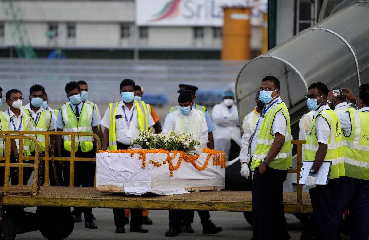 Sri Lankan air port workers stand next to a casket carrying remains of Priyantha Kumara, a Sri Lankan employee who was lynched by a Muslim mob in Sialkot last week after unloading it from an aircraft in Colombo, Sri Lanka, Monday, Dec. 6, 2021. (AP Photo/Eranga Jayawardena)