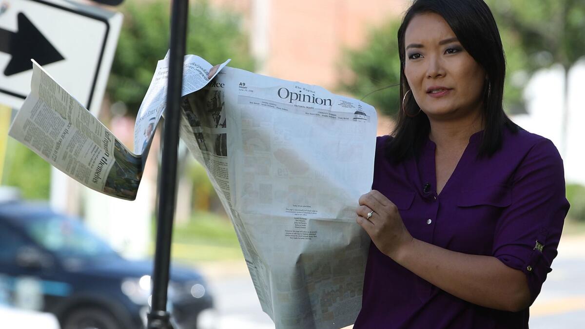 Television reporter Heidi Zhou-Castro holds up the opinion page of the Capital that was left blank the day after five people were shot and killed by a gunman at the newsroom.