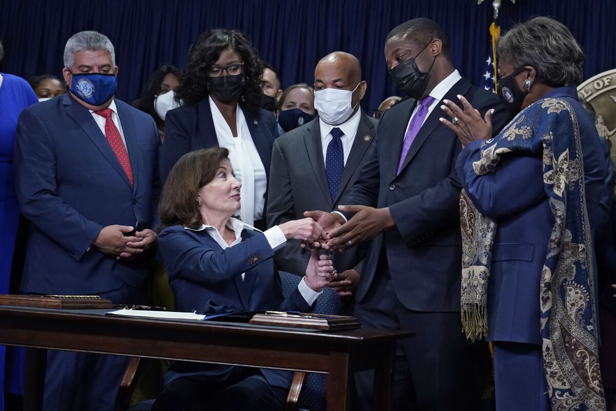 New York Gov. Kathy Hochul, seated, hands the first pen, during the signing of the "Less is More" law, to Lt. Gov. Brian Benjamin during ceremonies in the governor's office, in New York, Friday, Sept. 17, 2021. New Yorkers will be able to avoid jail time for most nonviolent parole violations under a new law that will take effect in March 2022, and largely eliminates New York's practice of incarcerating people for technical parole violations. (AP Photo/Richard Drew)