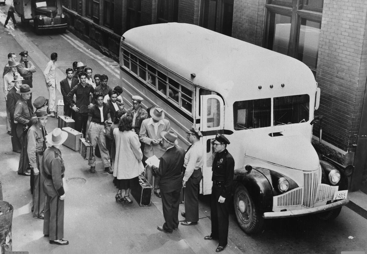 People line up to board a bus watched by several law enforcement officers