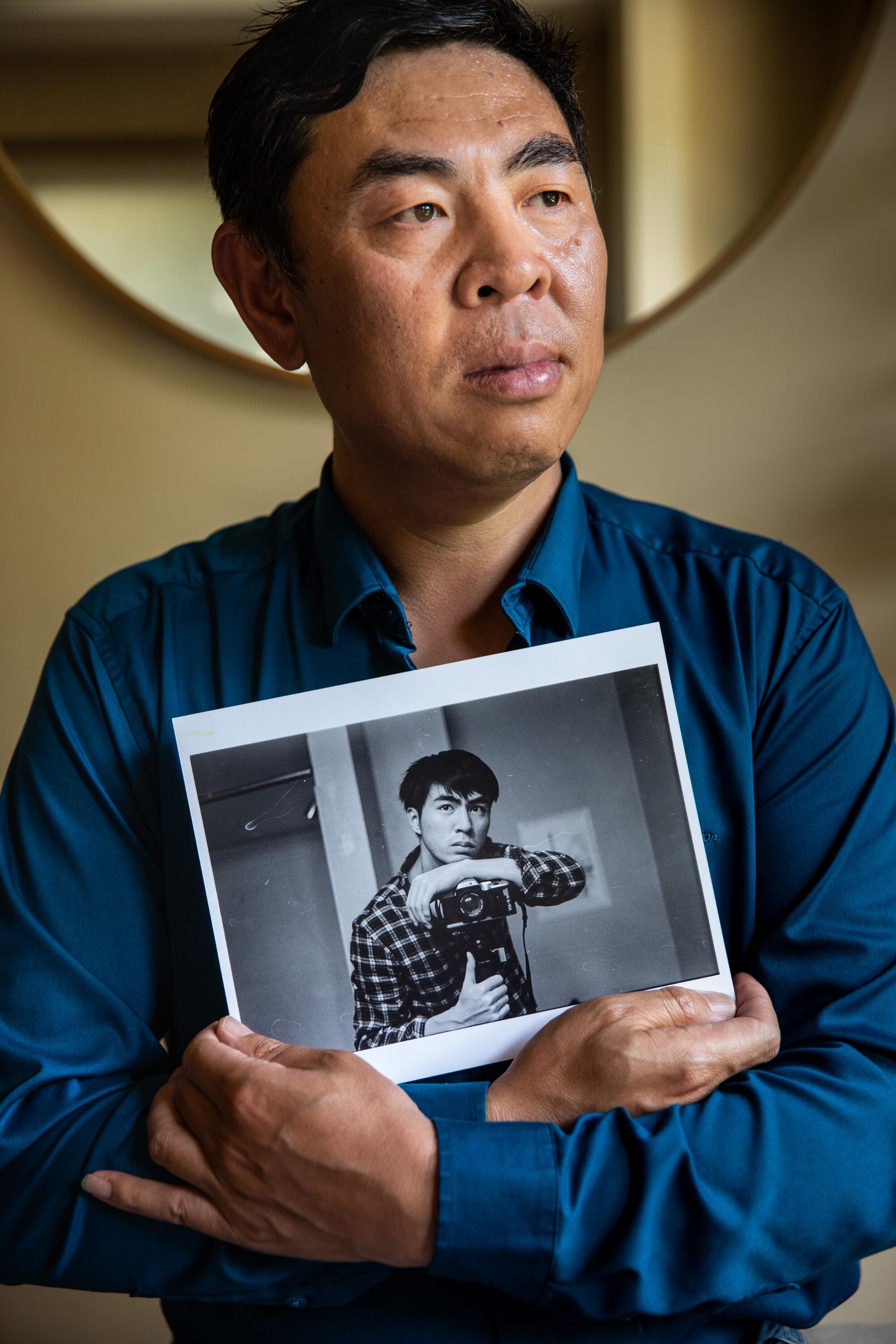 A man holds a black-and-white photo of his son.