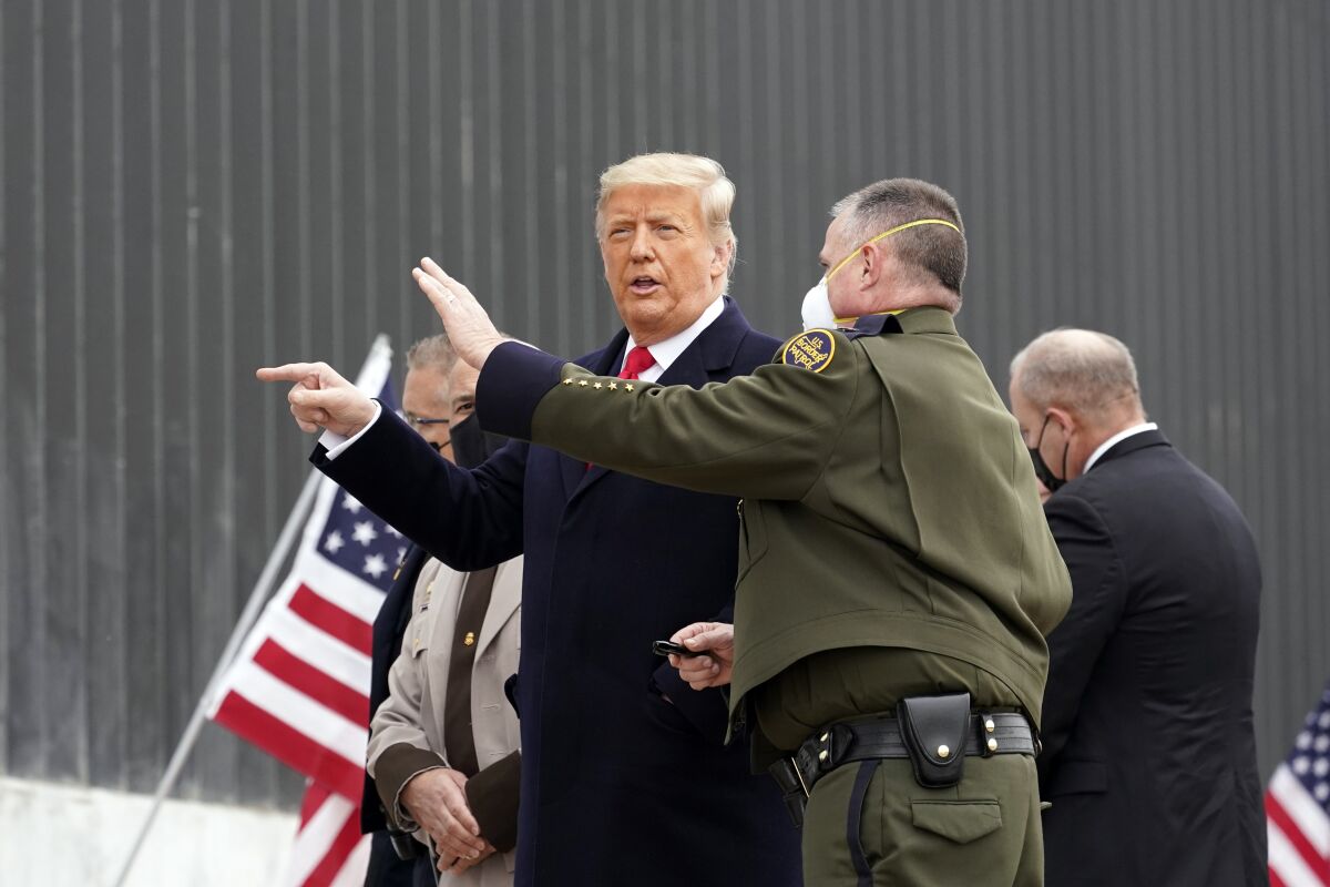 Trump, unmasked, speaks with a masked Border Patrol officials.