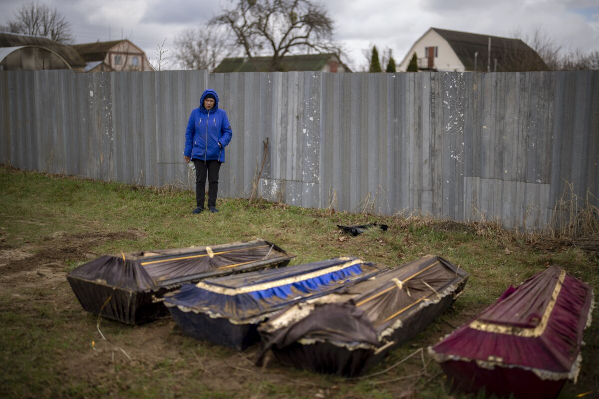Ira Slepchenko stands next to coffins during an exhumation of a mass grave in Mykulychi, Ukraine.