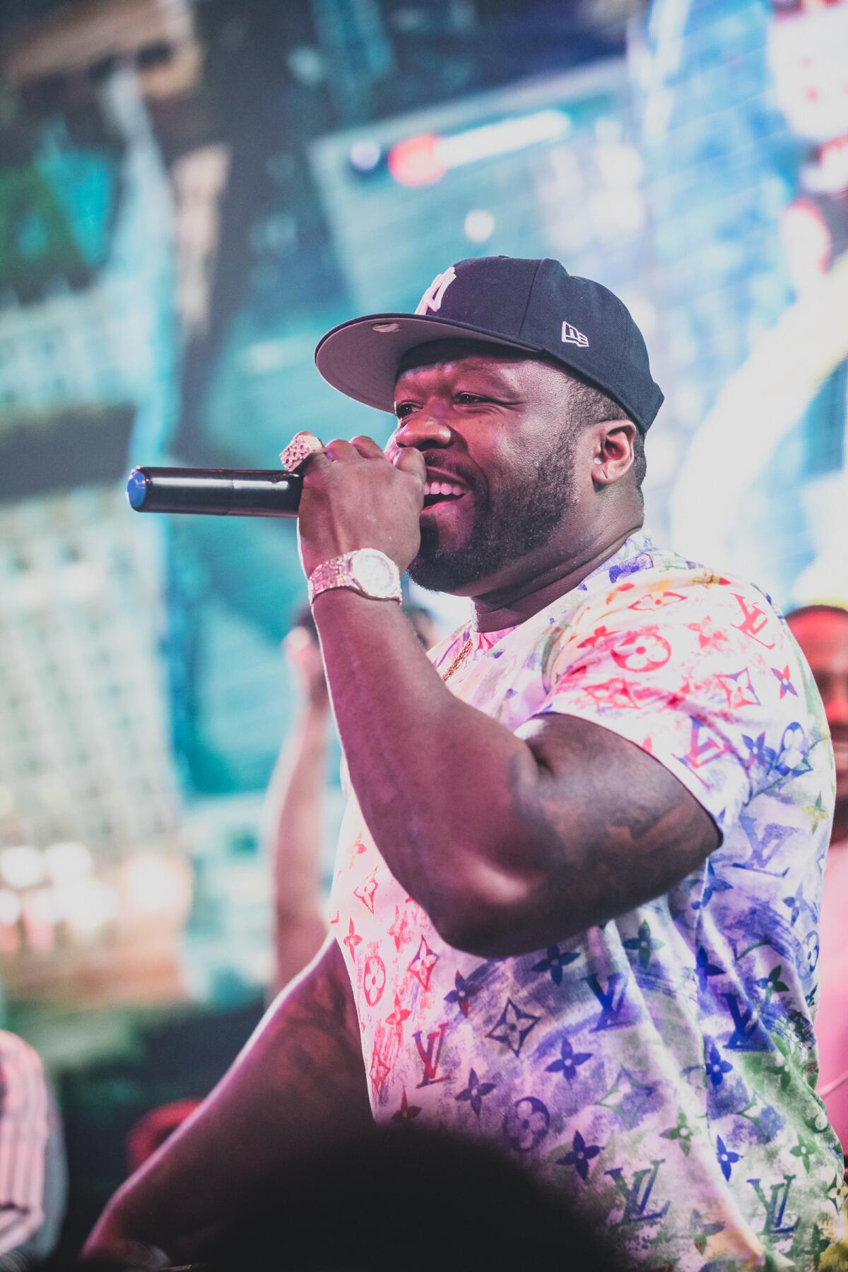Rapper 50 Cent holds a mic as he raps on stage wearing a baseball cap. 