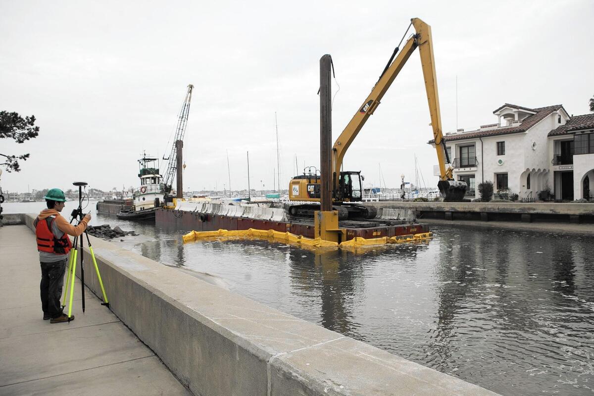 Alfredo Gutierrez, left, with Associated Pacific Constructors, uses surveyors equipment with GPS technology to monitor the dredging in the Grand Canal between Balboa Island and Little Balboa Island on Thursday.