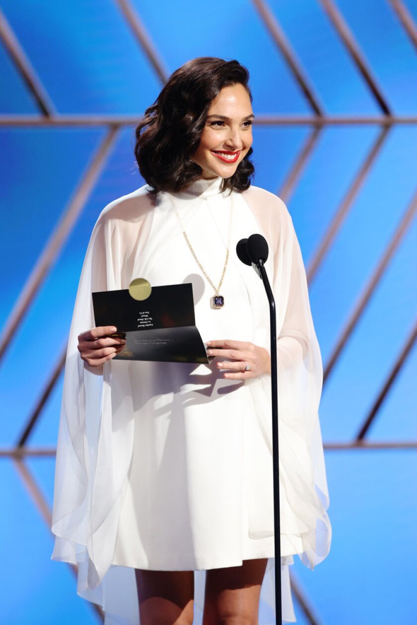 Gal Gadot holds an awards envelope and smiles.