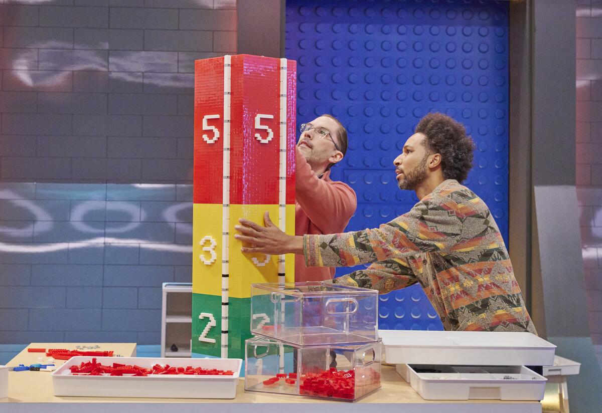 Two men construct a numbered tower out of Lego in primary colors