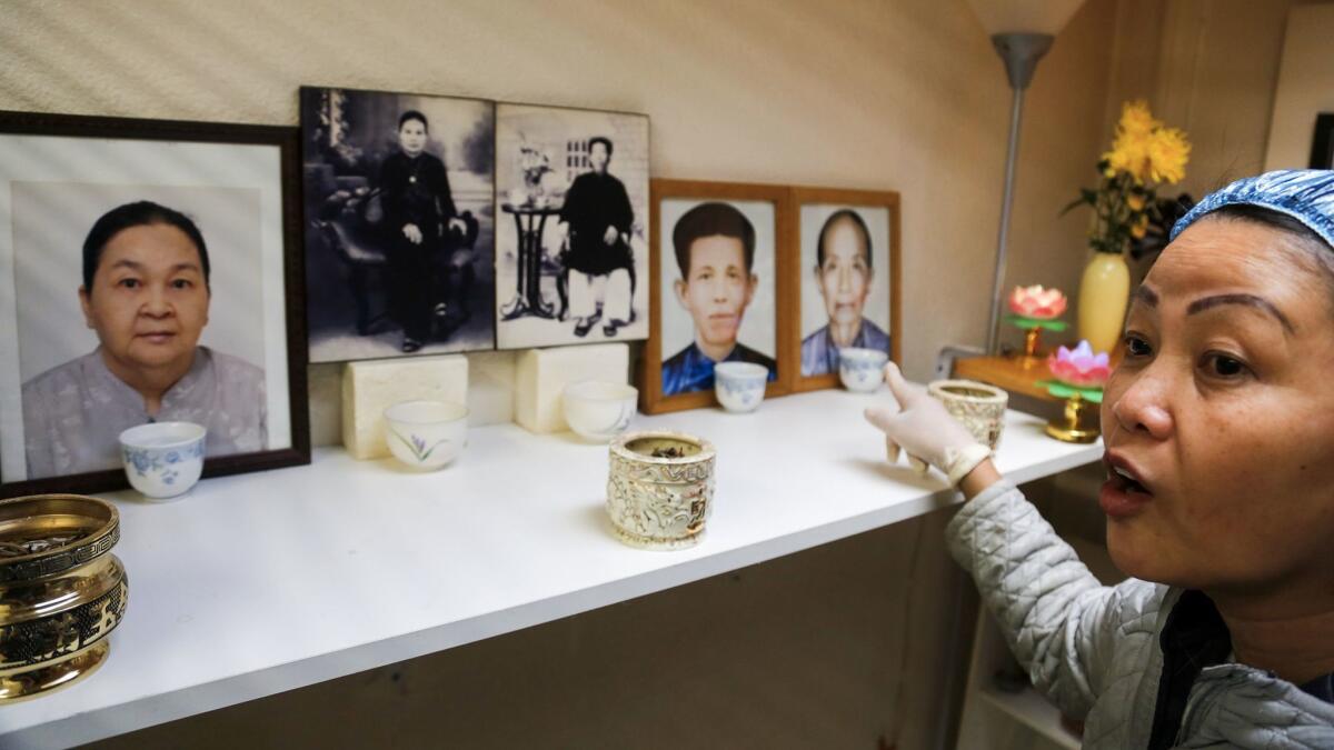 Hue Phan points to pictures of her and her husband's parents and grandparents arranged for a home shrine. (Mark Boster / Los Angeles Times)
