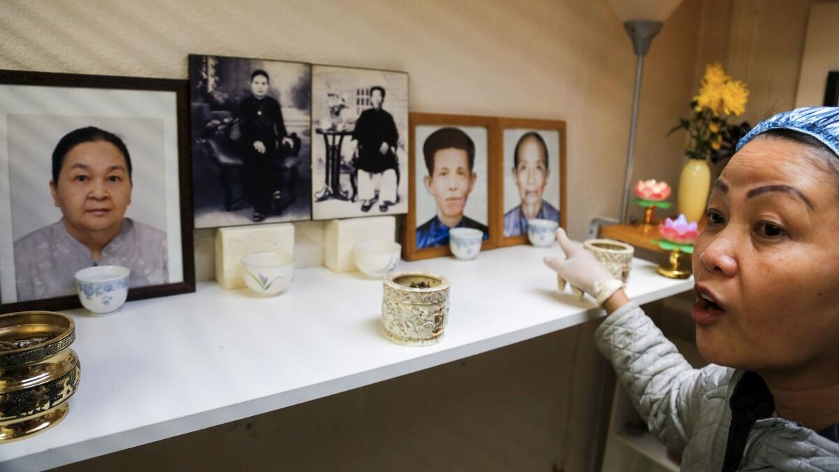 Hue Phan points to pictures of her and her husband's parents and grandparents arranged for a home shrine.