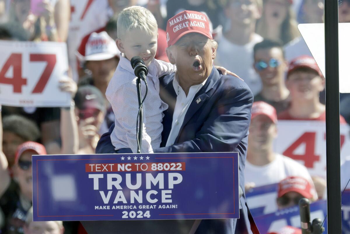 Donald Trump holds his young grandson while standing behind a lectern.