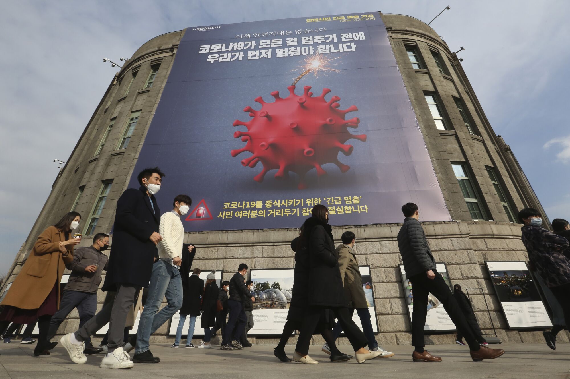 People wearing face masks walk past a coronavirus safety banner ad advising an enhanced social distancing campaign in Seoul.