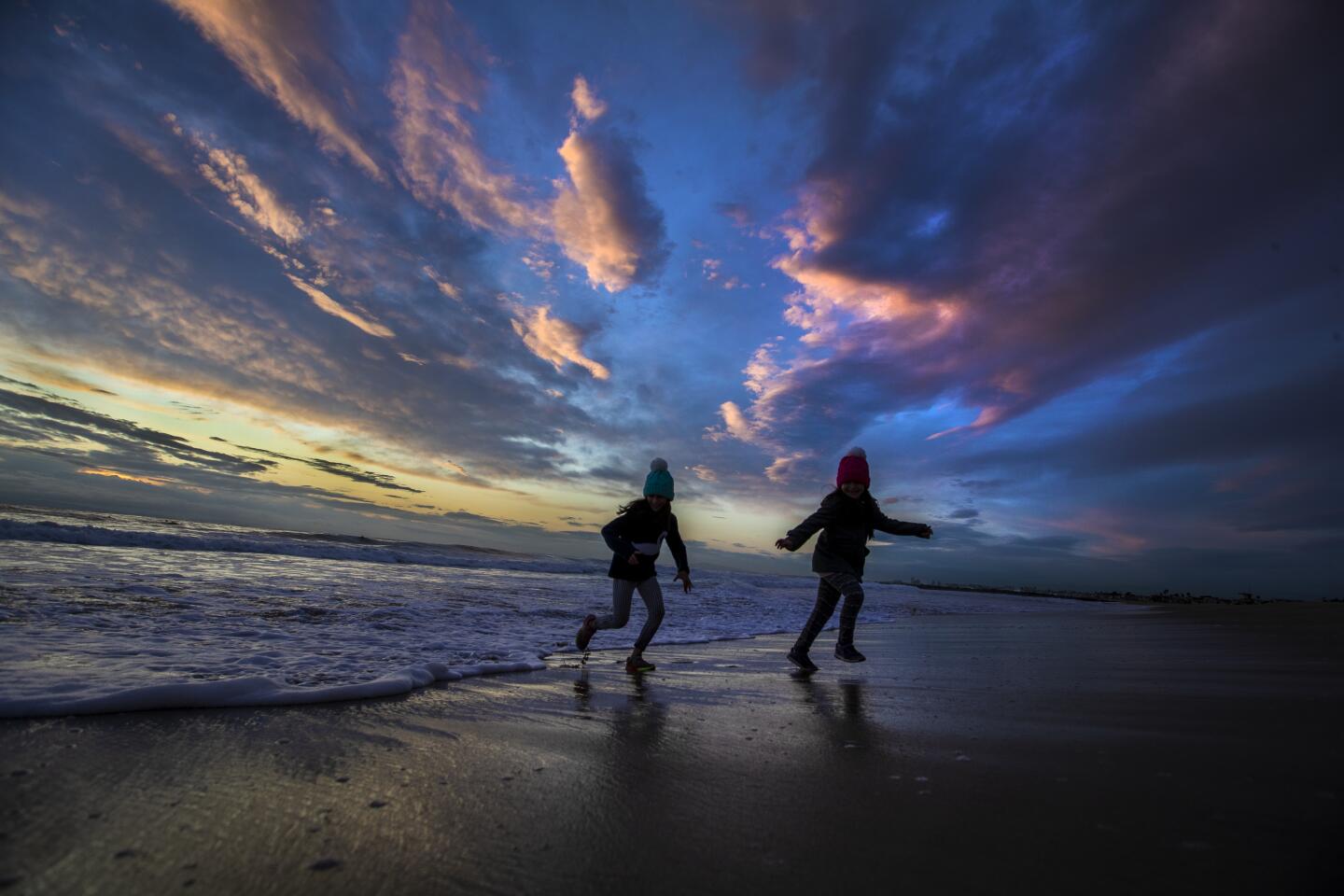 Chi Chi Hakimi, 9, left, and Darya Hakimi, 8, are silhouetted by the sky at dusk as they run from the waves in between rain showers in Newport Beach, Calif., on Nov. 20, 2019.