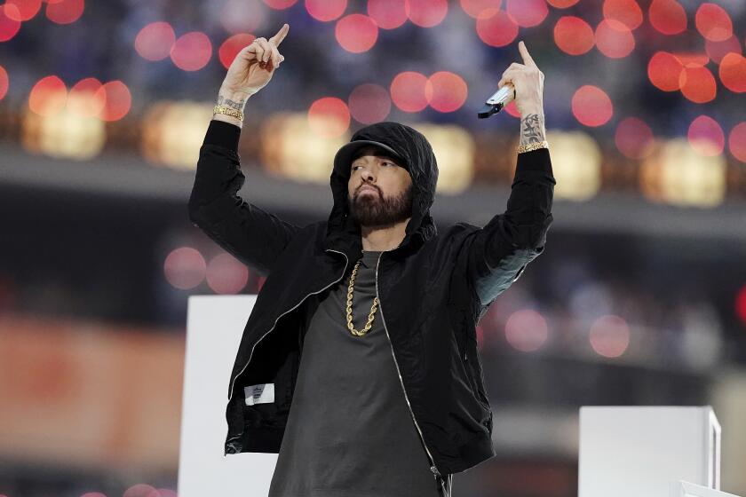 A man in a black hoodie raises his hands while holding a microphone