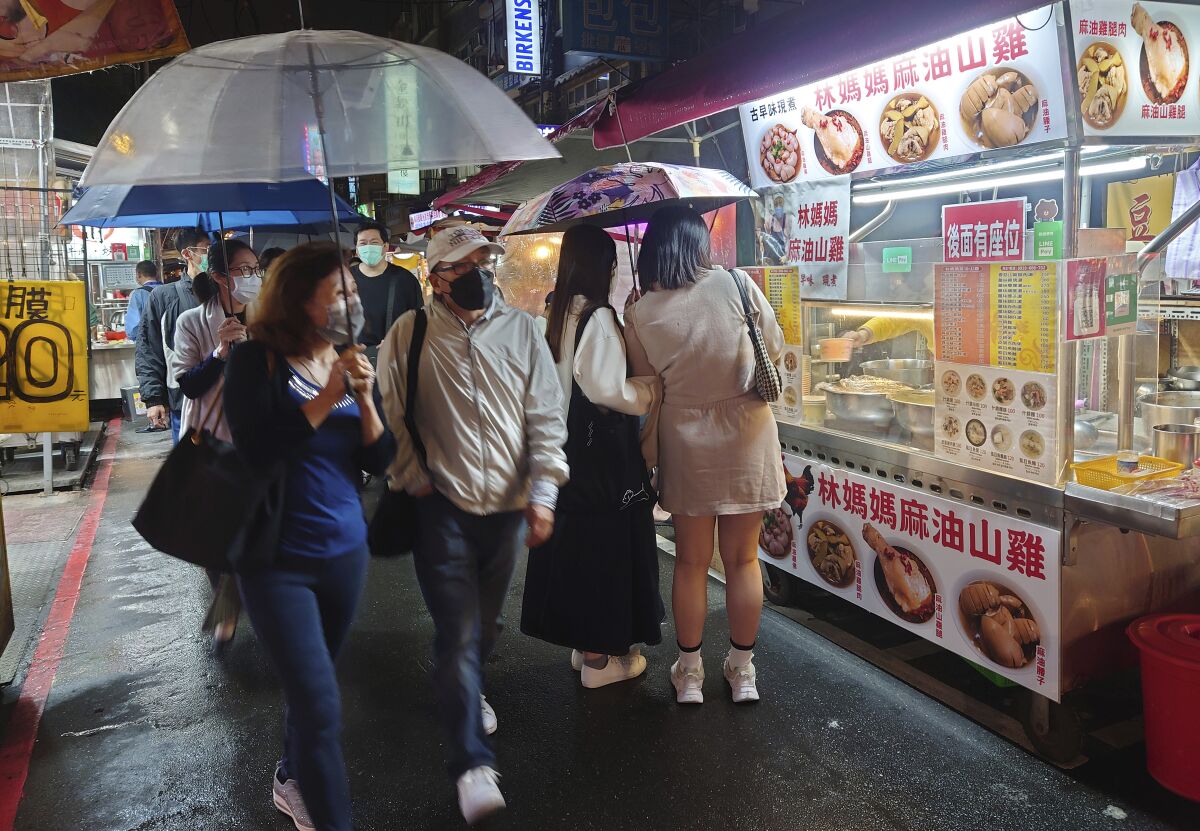 People wear face masks while walking through a night market in Taipei.