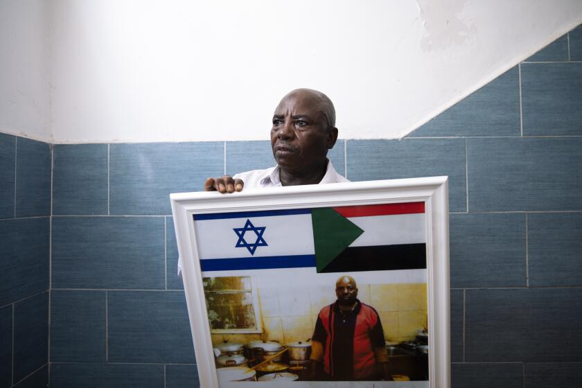 Sudanese migrant Attom Alialdom 56, poses for a photo as he holds a photo of his old restaurant decorated with Sudanese and Israeli flags, outside his house in south Tel Aviv, Israel, Sunday, Oct. 25, 2020. After Israel and Sudan agreed this month to normalize ties, some 6,000 Sudanese migrants in Israel are again fearing for their fate. Israel has long grappled with how to deal with its tens of thousands of African migrants. (AP Photo/Oded Balilty)