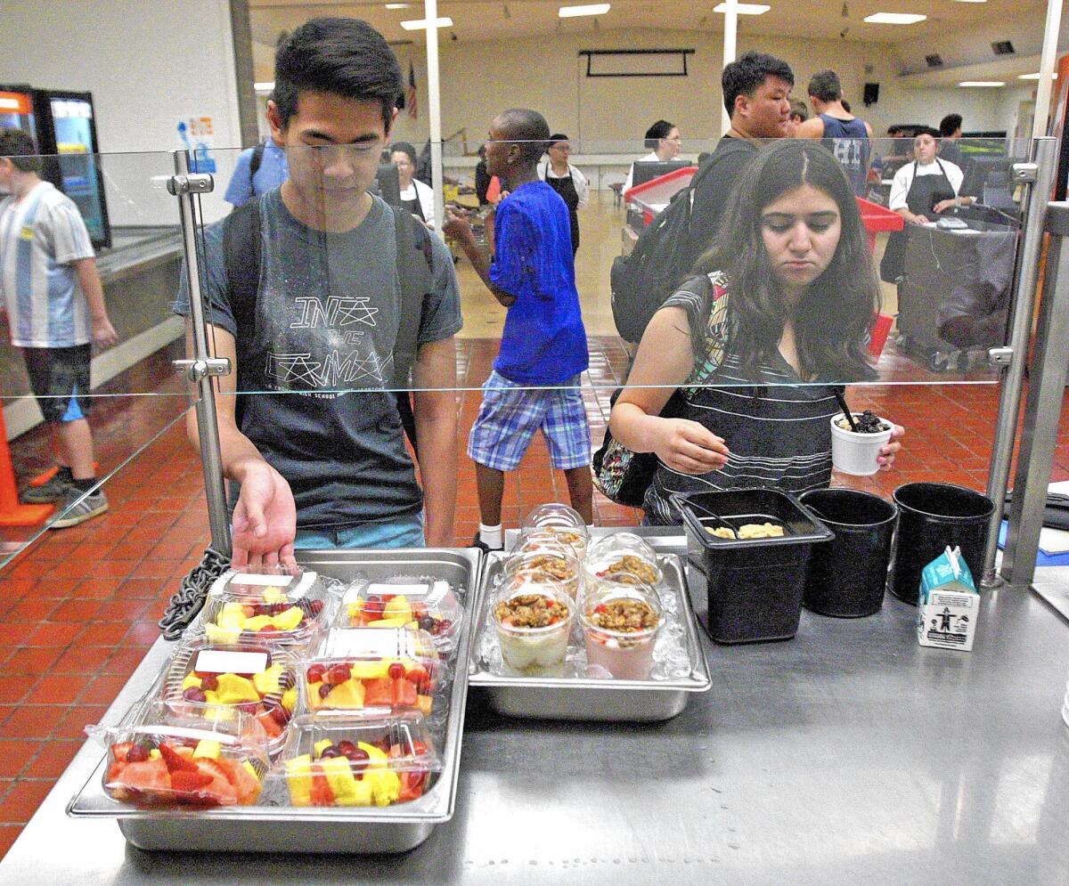La Cañada High School student Bryan Dohi, 17, picks up a container of fresh fruit, and Ashley Medina, 15, tops off a cup of oatmeal in the cafeteria.