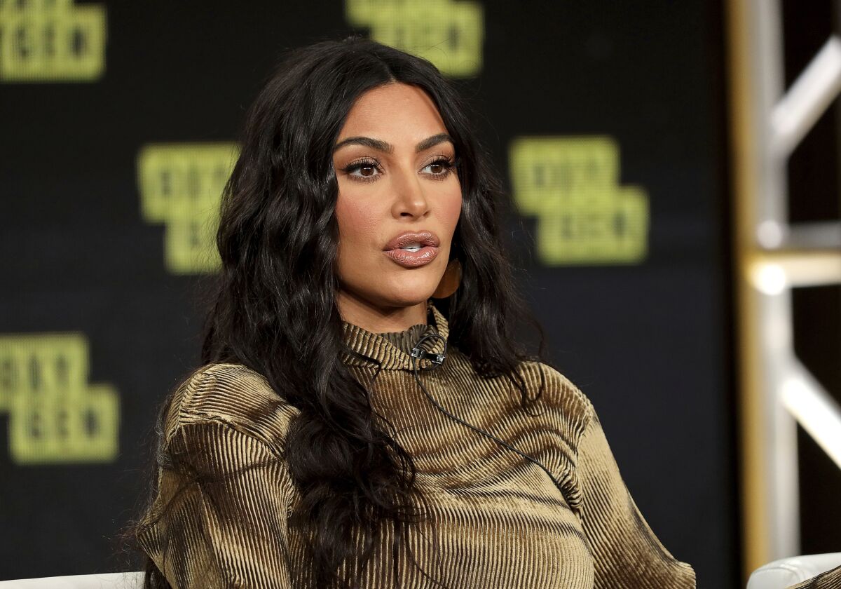 A woman with long, dark hair sits and speaks.