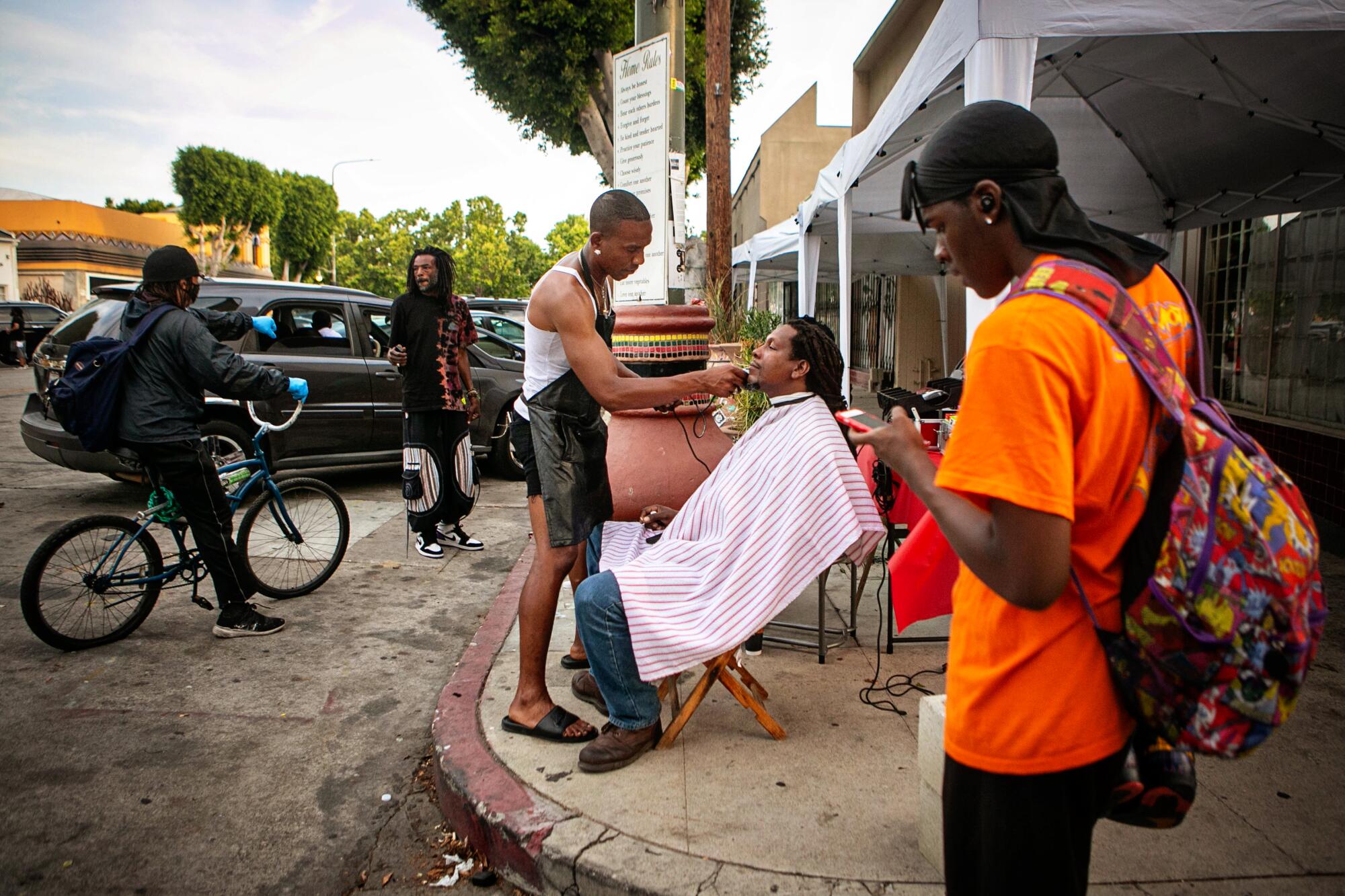 A man in a black apron gives a seated man a trim