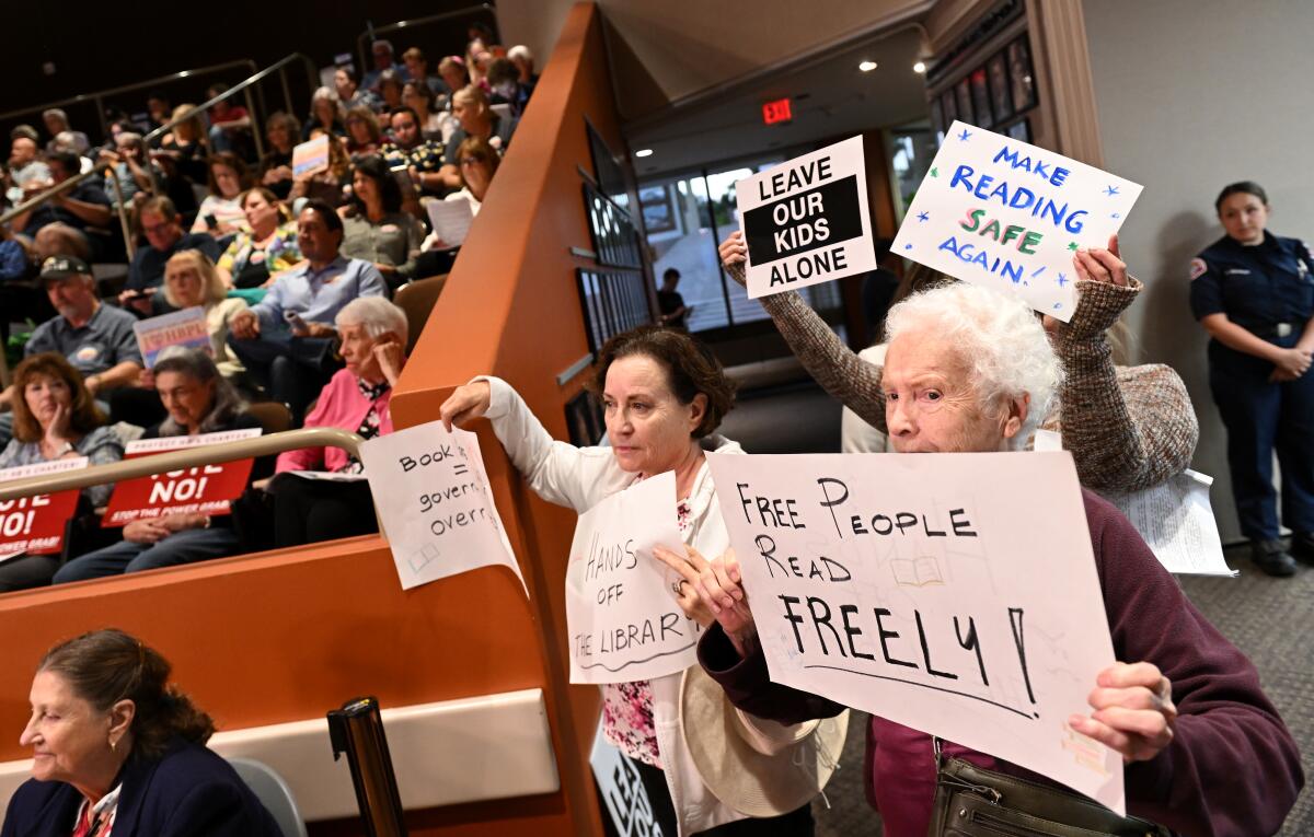 Opponents of book bans hold signs at a City Council meeting.