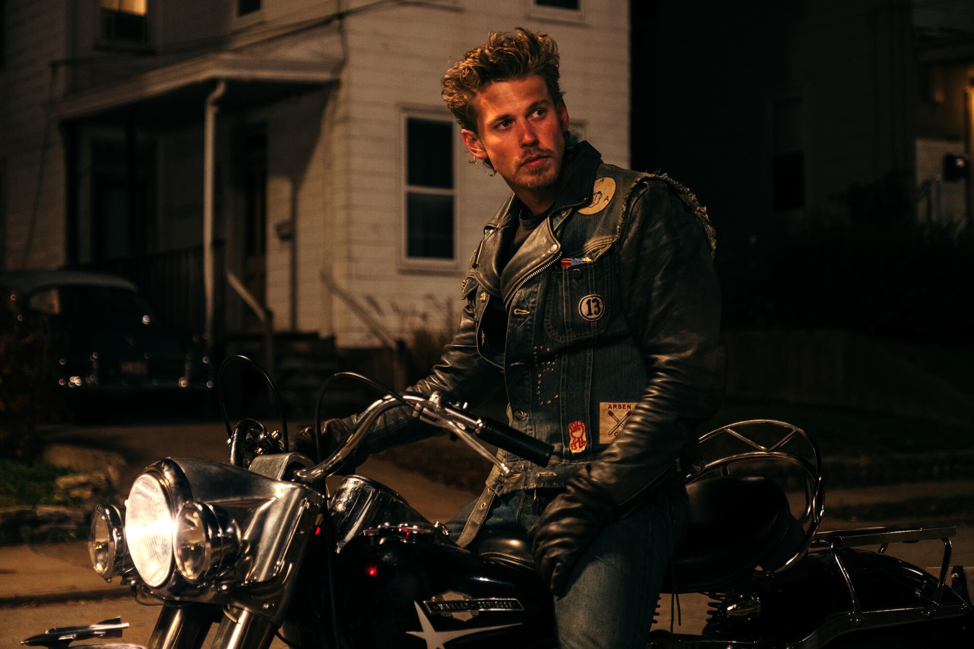 A man in a leather jacket sits on a motorcycle.