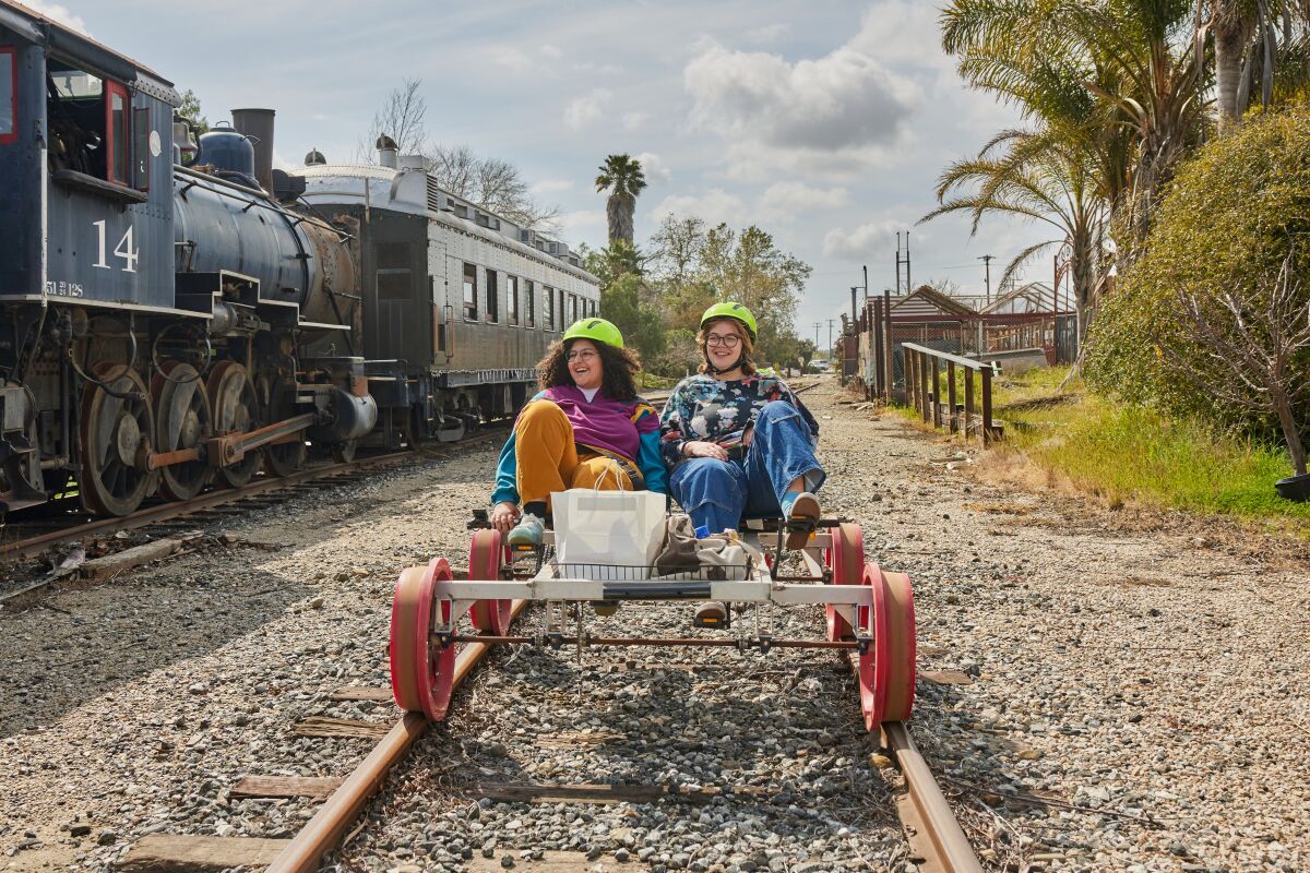 Two people wearing helmets seated on a railbike.