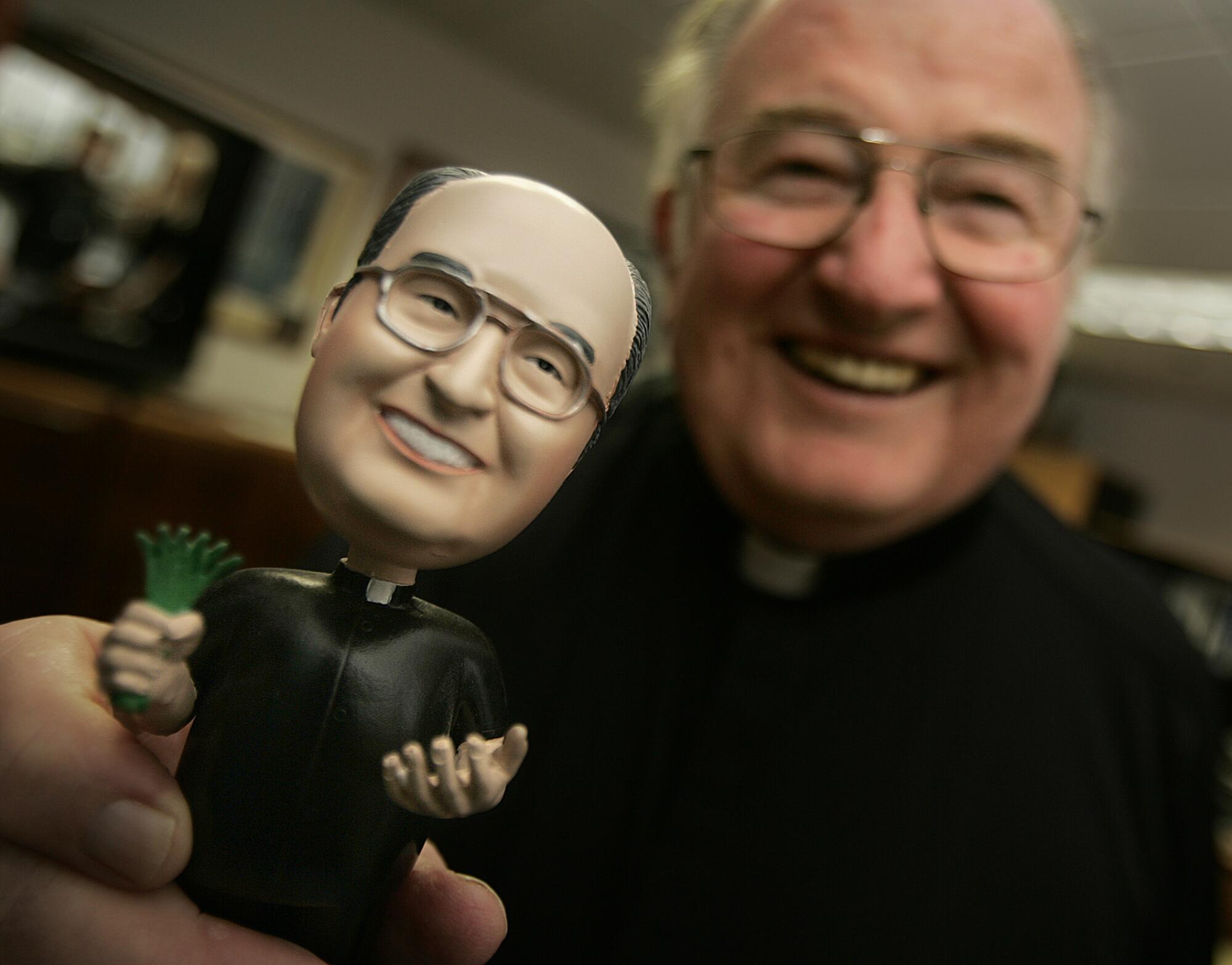 Father Joe Carroll holds a bobblehead doll of himself