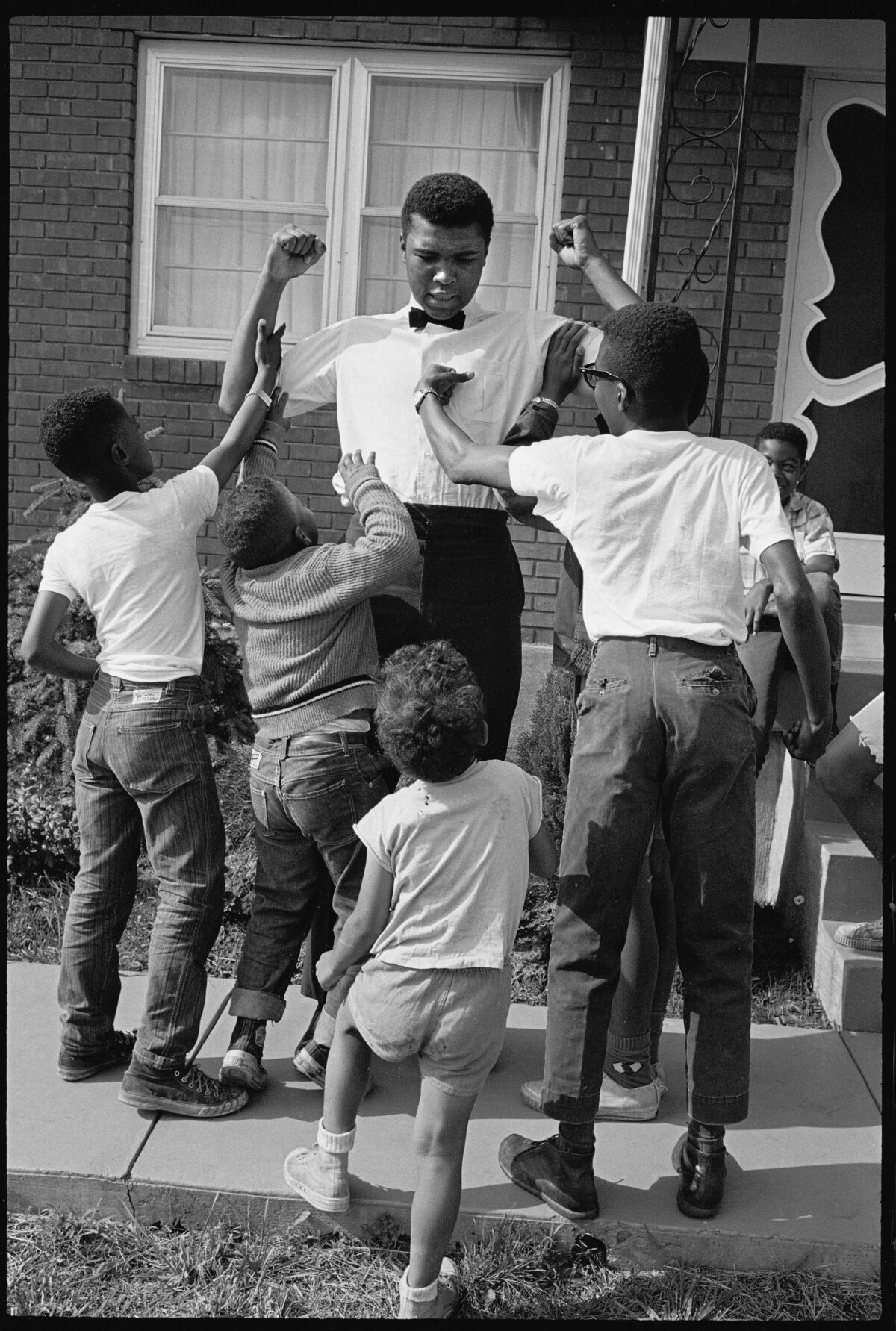 A black-and-white image of children punching and grabbing boxer Muhammad Ali.
